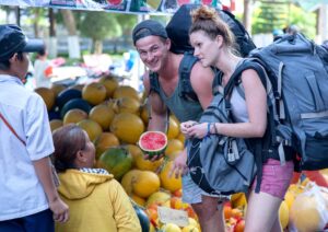 mochileiros escolhendo economizar comprando em feira local enquanto viajam pelo brasil - Mochilão - O guia completo de como viajar barato pelo Brasil